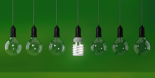 Energy saving light bulb is standing out from the crowd over green background. Energy efficiency concept. Horizontal composition with copy space.