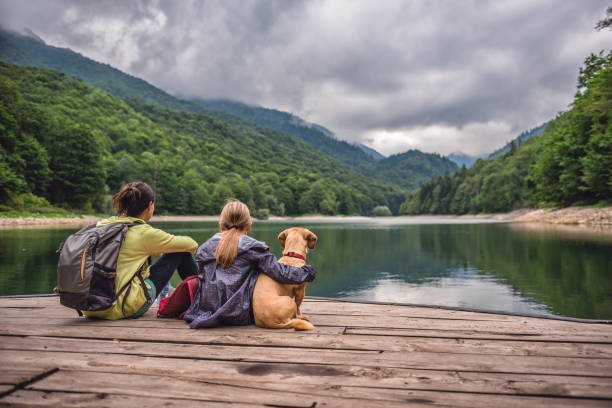 mutter und tochter mit einem hund ruht auf einem pier - ökotourismus stock-fotos und bilder