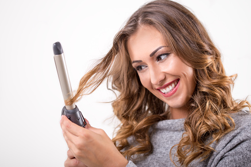 Happy beautiful woman curling her hair while smiling