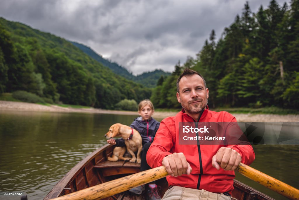 Father and daughter with a dog rowing a boat Father and daughter with a small yellow dog rowing a boat on a mountain lake Active Lifestyle Stock Photo