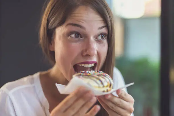 25 years old businesswoman after work in restaurant. She is enjoying eating doughnuts