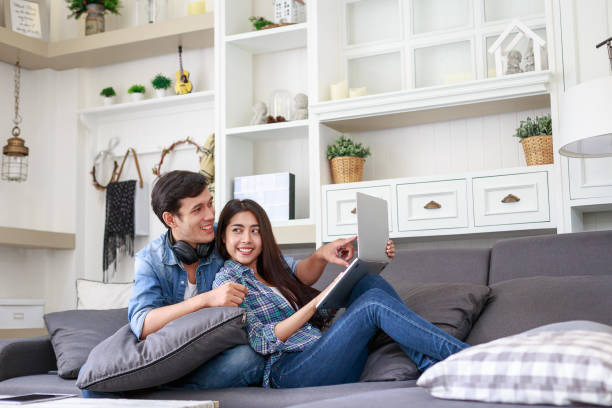 istock Young Asian couple relaxing together on sofa and using laptop computer at home in the living room 851966110