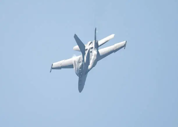 F-18 Hornet in a high G maneuver, with condensation trails forming at the wing’s root, in strong light