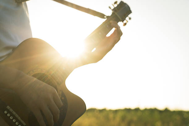 closeup of man hands playing guitar in field against sunbeam.