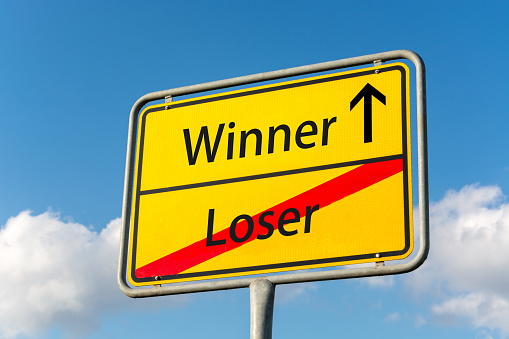 Yellow street sign with winner ahead leaving loser behind close up