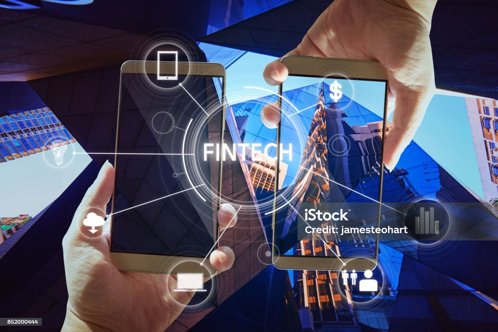 "Fintech" word on digital virtual screen with two businessman hands holding smartphones background. Financial Technology Stock Photo