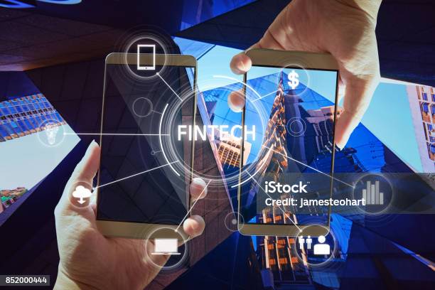Fintech Word On Digital Virtual Screen With Two Businessman Hands Holding Smartphones Background Stock Photo - Download Image Now