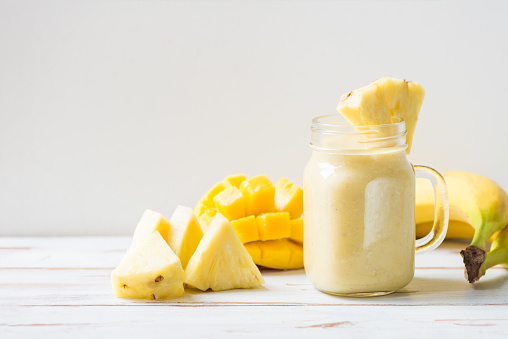 Mango, Banana, Pineapple and Oatmeal Smoothie in the Jar with Ingredients nearby on the Light Background