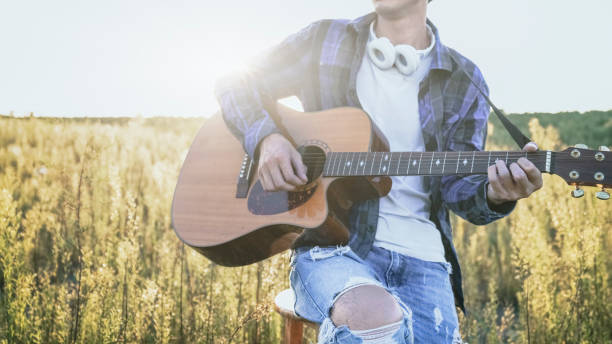 istock young man sitting in grassy field playing guitar 852002620