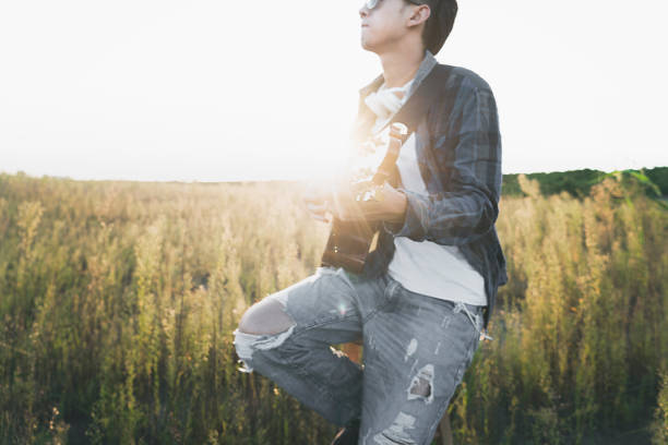 young man sitting in grassy field playing guitar.