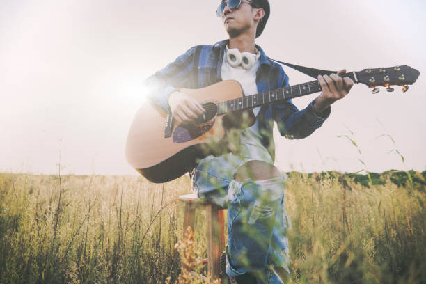istock young man sitting in grassy field playing guitar 852003326