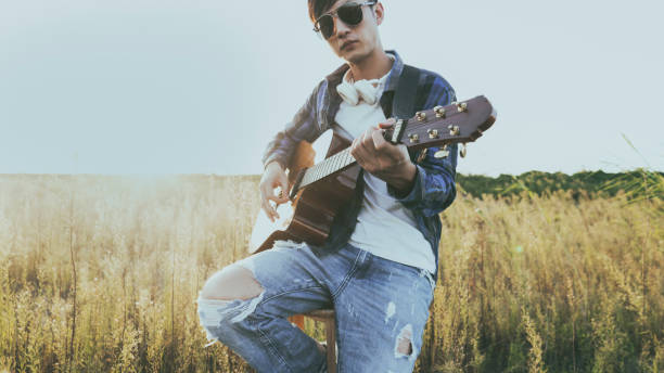 istock young man sitting in grassy field playing guitar 852003678