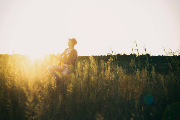 istock young man sitting in grassy field playing guitar 852003948