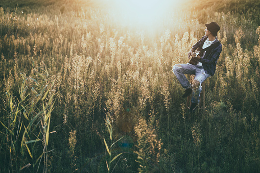 young man sitting in grassy field playing guitar.