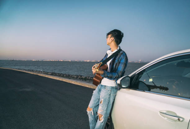 istock young male playing guitar leaning on car hood 852007562