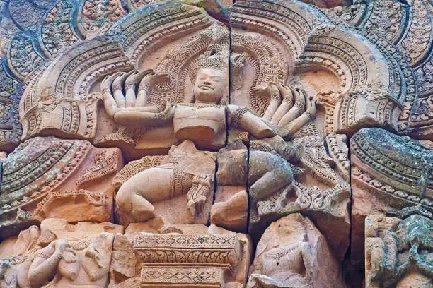 Ancient Cambodian Stone carving of god with ten hand dancing form on wall of temple complex set in Phanom Rung Historical Park, Buriram province, Thailand