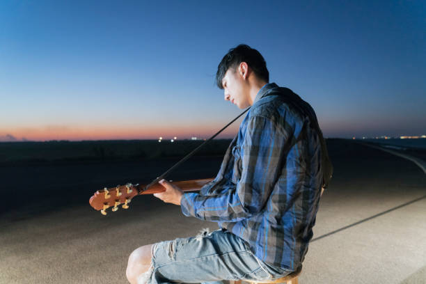 young guitarist playing acoustic guitar at urban waterfront.