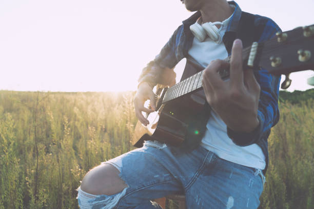 istock young man sitting in grassy field playing guitar 852016164