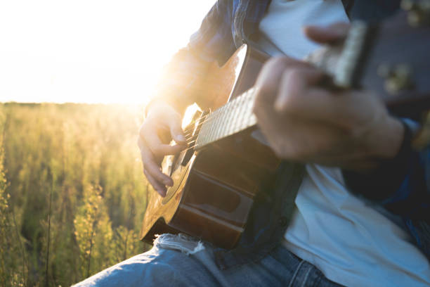 istock young man sitting in grassy field playing guitar 852016264