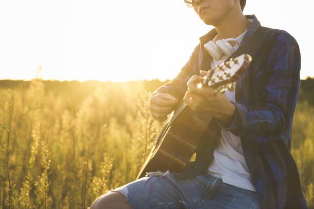 istock young man sitting in grassy field playing guitar 852016946