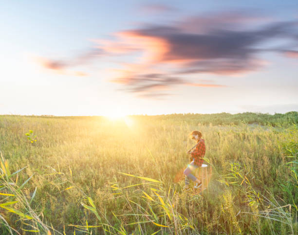 young female guitarist playing guitar in grassy field.