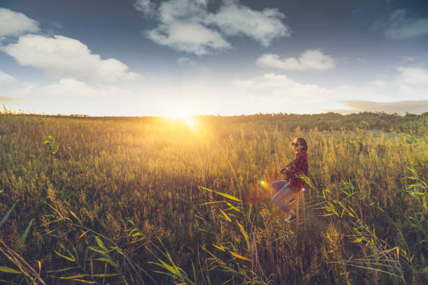 young female guitarist playing guitar in grassy field.