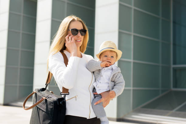 mutter zur arbeit zu gehen und das gespräch am telefon mit baby in die hände - working mother working mother balance stock-fotos und bilder