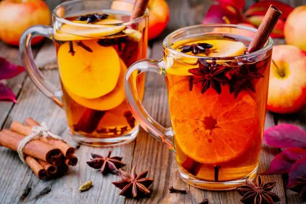 Hot mulled apple cider with cinnamon sticks, cloves and anise on wooden background