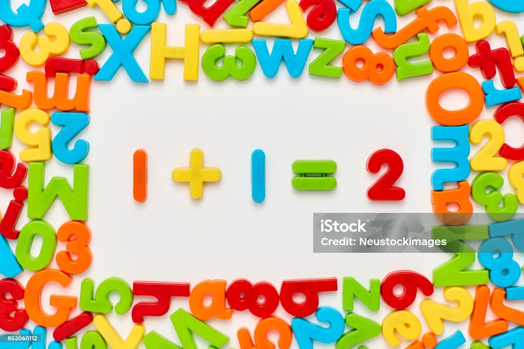 Overhead view of one plus 1 equals two on white Overhead view of one plus one equals two surrounded with colorful alphabets and numbers on white background. Flat lay of multi colored plastic toys arranged in frame. Image is representing mathematical equation. Letter Magnet Stock Photo