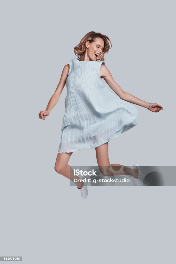 Going crazy. Full length of playful young woman smiling while jumping against grey background Women Stock Photo