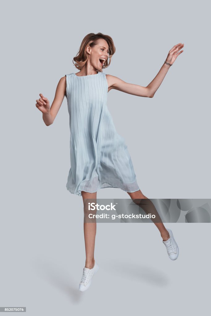 Beauty in motion. Full length of playful young woman gesturing and keeping mouth open while jumping against grey background Women Stock Photo