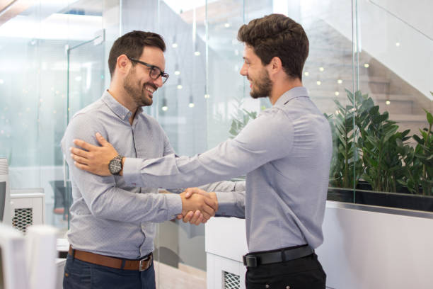 istock Two smiling businessmen shaking hands together while standing in modern office. 852088566