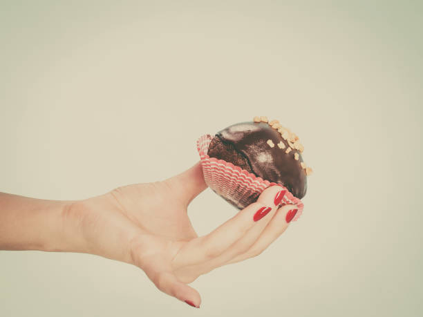Woman hand holding chocolate cupcake about to bite