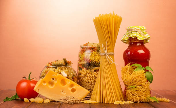 istock Bound spaghetti, nest of thin vermicelli, two jars with different pasta, bottle of ketchup, tomatoes, cheese on red. 852093530