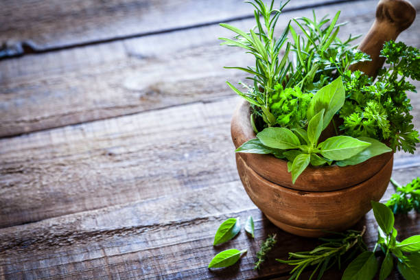 Mortar and pastle with fresh herbs for cooking on rustic wooden table High angle view of an old wooden mortar filled with fresh organic herbs for cooking shot on rustic plank.. The mortar is at the right of an horizontal frame leaving useful copy space for text and/or logo at the left. Predominant colors are brown and green. DSRL studio photo taken with Canon EOS 5D Mk II and Canon EF 100mm f/2.8L Macro IS USM mortar and pestle stock pictures, royalty-free photos & images