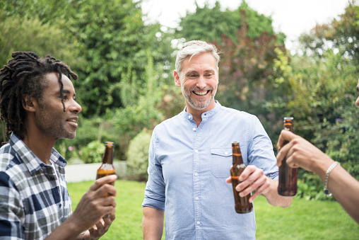 Candid portrait of small group of friends enjoying beer, mature man with blue shirt and beard smiling and looking away