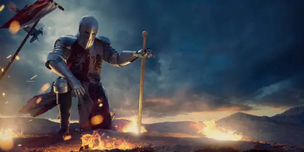 A knight in a full suit of armour, and tabard kneeling with one hand on knee and other resting on sword. The warrior is on rocky high ground surround by small fires of burning debris., with medieval battle flag in the ground behind him, under a dramatic, dark, stormy evening sky.