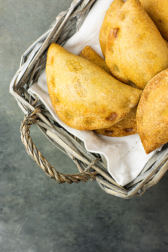 Homemade freshly baked Empanadas Turnover Pies with pisto vegetable cheese filling in tomato sauce in wicker basket. Spanish pastry. Dark concrete stone background. Top View Minimalist. Copy Space.