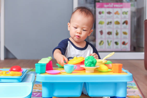 Cute little Asian 18 months / 1 year old toddler baby boy child having fun playing alone with cooking toys in living room at home, stock photo