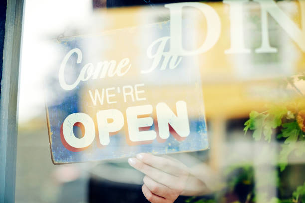 istock Young saleswoman hanging open sign seen through window 852153948