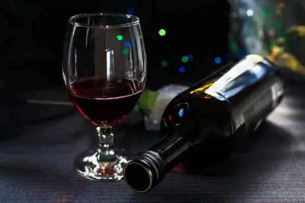 Glass of red wine and bottle of wine, against a dark background.