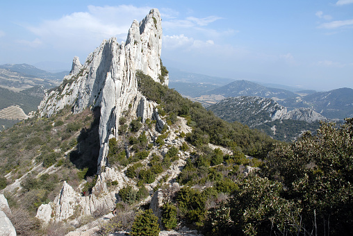 Dentelles de montmirali mountain range in Provence, France, seen from place near the peak with panoramic landscape in the background and forest in foreground, blue sky, sunlight