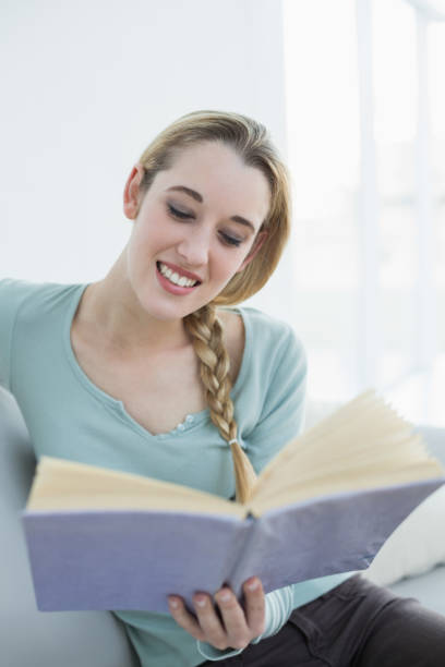 istock Cheerful beautiful woman reading a book while sitting on couch 852196426