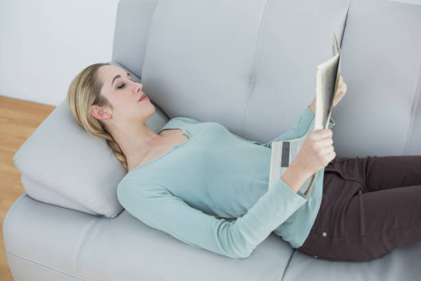 istock Slender natural woman reading newspaper lying on couch 852197140
