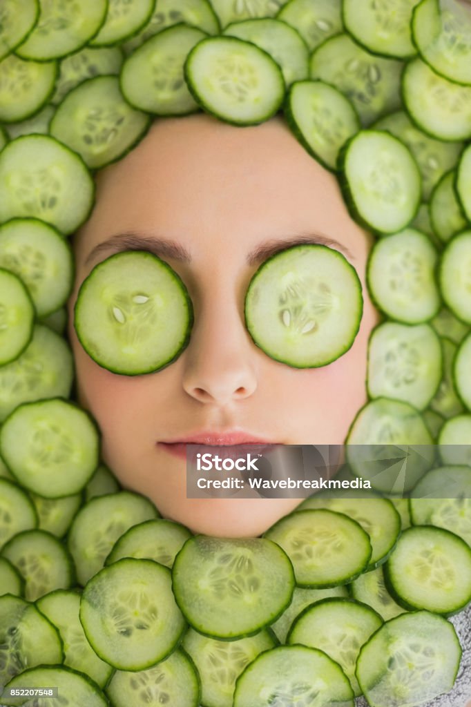 Beautiful woman with facial mask of cucumber slices on face Close up of a young beautiful woman with facial mask of cucumber slices on her face at spa salon Cucumber Stock Photo