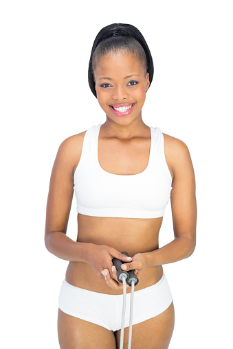 Fit smiling woman in sportswear holding jump rope against white background