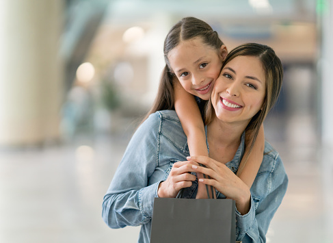 Portrait of a happy mother and daughter at the shopping center holding bags and looking at the camera smiling