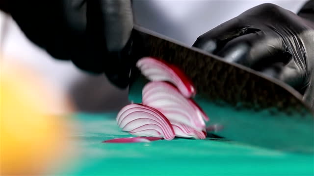 Chef cuts up purple onion using knife to slice. Close up