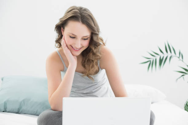 istock Smiling casual brunette looking at laptop in bed 852213988