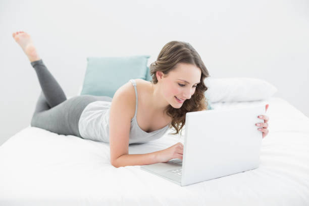 istock Smiling casual brunette using laptop in bed 852214242